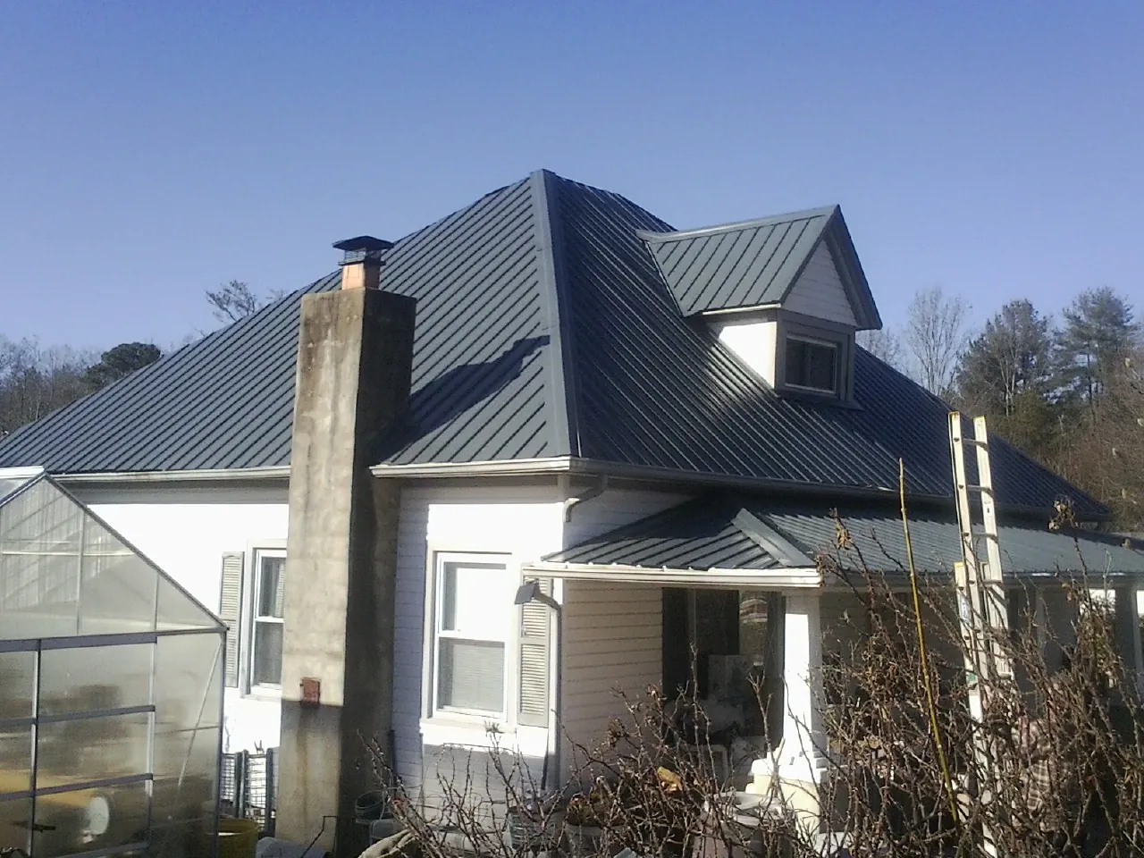 Dark blue standing seam metal roof on a white farmhouse with dormer — Slate & Tile Roof Repair by Roofing Brothers in Oakpark