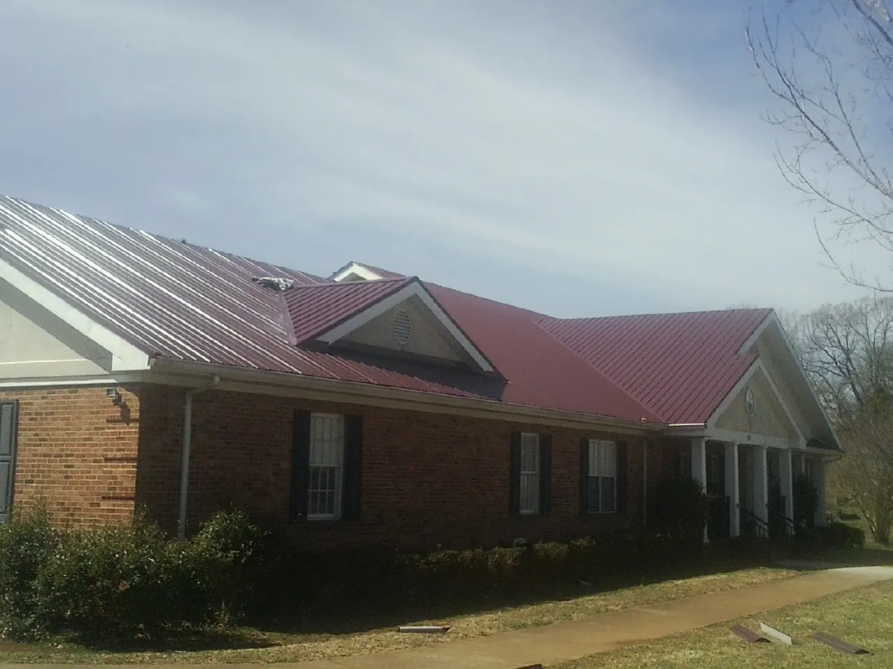 Red metal roof with gabled entries on a long brick building, from a Hail Damage Roof Repair job in Oakpark