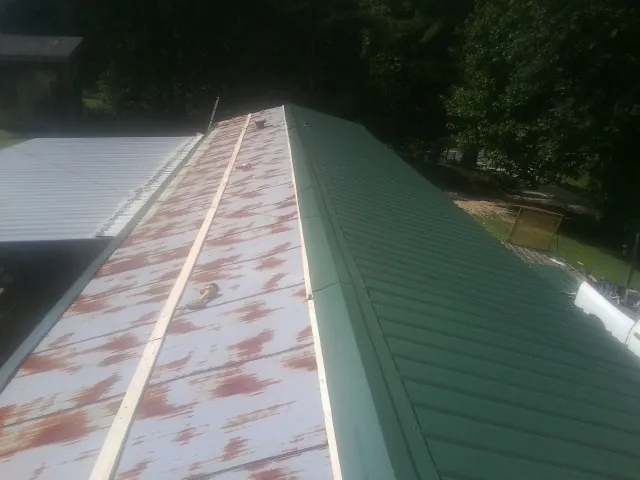 Old rusted panels beside newly installed green metal roofing — Wind Damage Roof Repair by Roofing Brothers in Oakpark