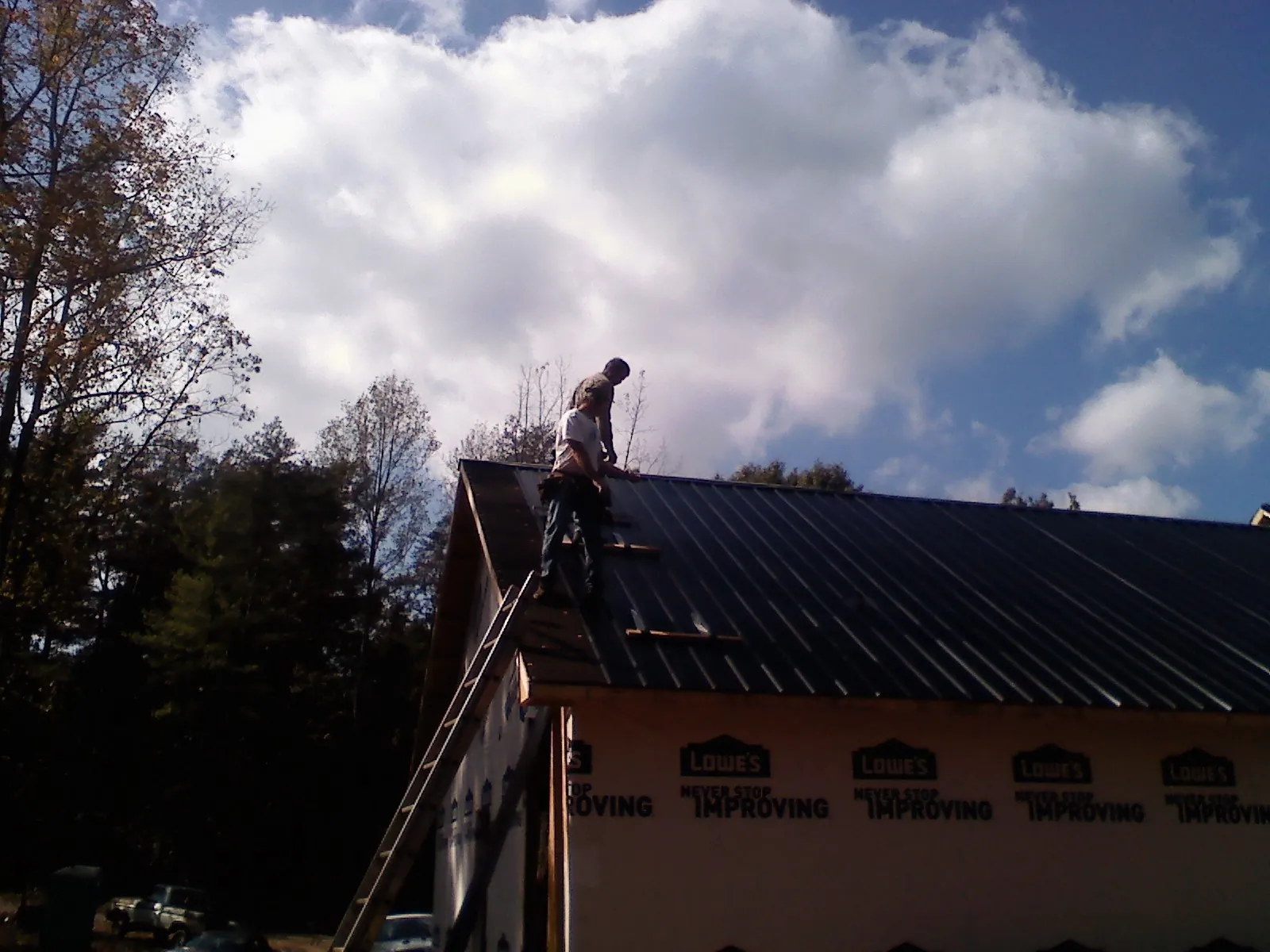 Roofer fastening dark metal panels high against a cloudy sky, from a Roof Inspection job in Oakpark