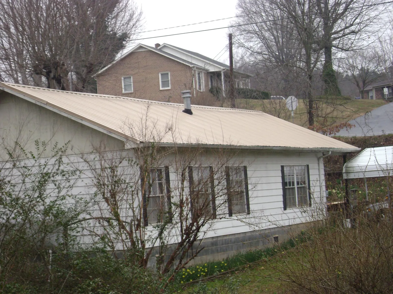 Tan metal roof on a white sided house set into a hillside — Commercial Roofing by Roofing Brothers in Oakpark