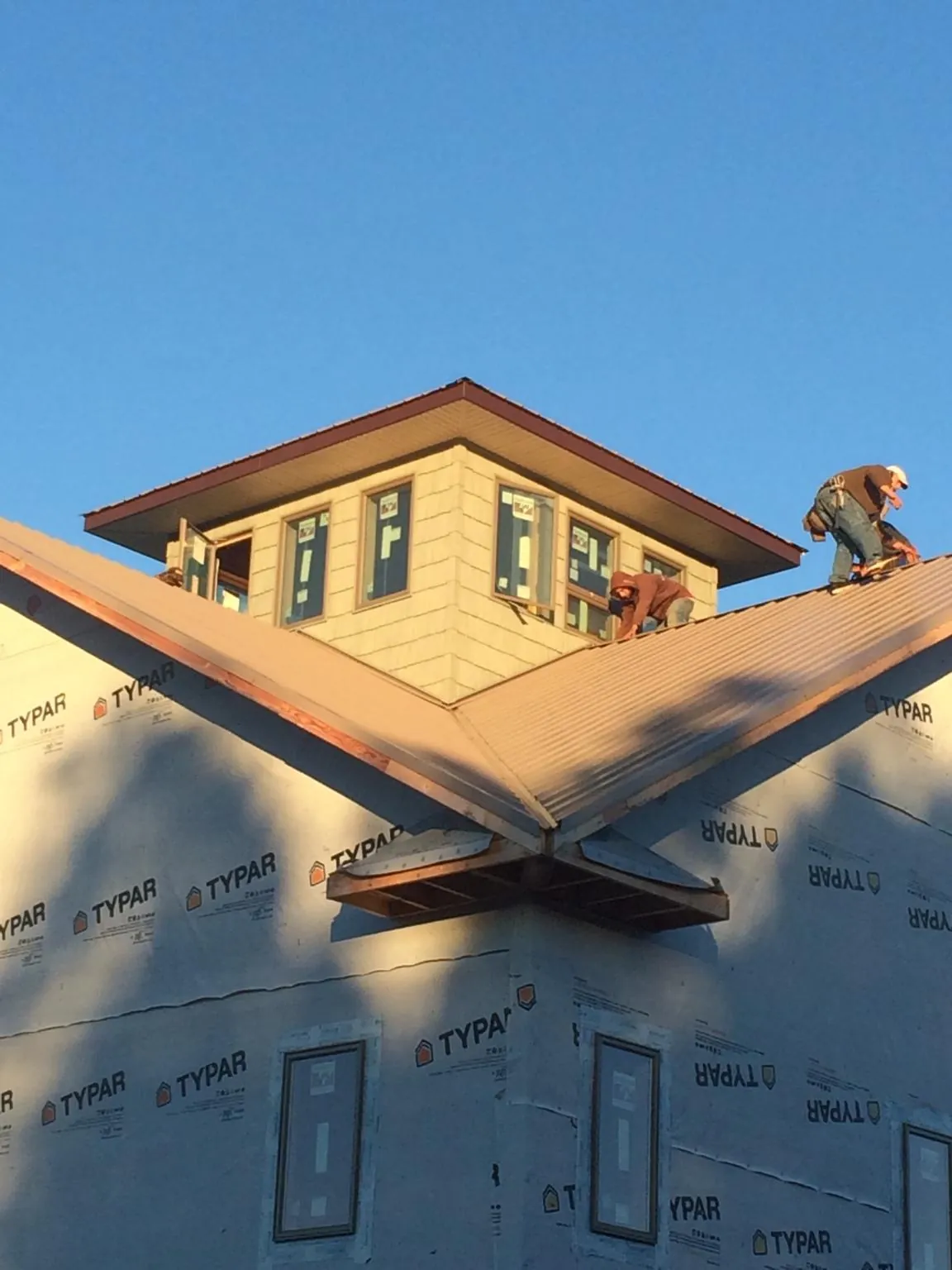 Roofers working around a rooftop cupola on a new metal roof at sunset in Oakpark